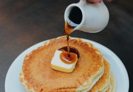 Syrup being poured over a stack of pancakes on a white plate.