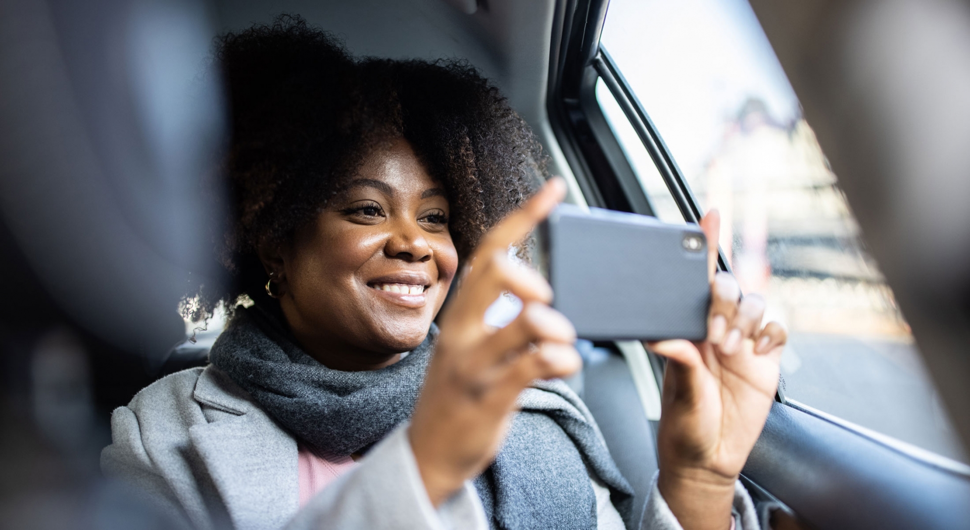 A woman taking pictures with her phone from a car back seat