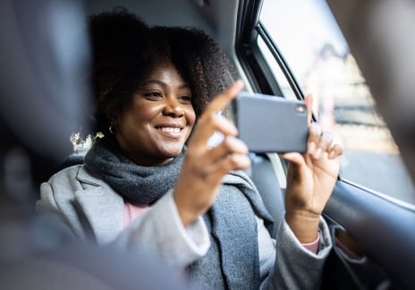 A woman taking pictures with her phone from a car back seat
