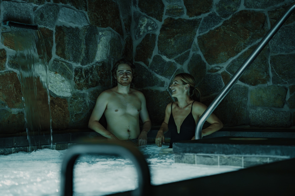 Couple relaxing in a stone-walled indoor hot tub.