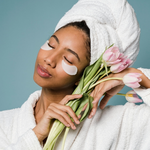 Woman in a bathrobe holding pink tulips to her face.