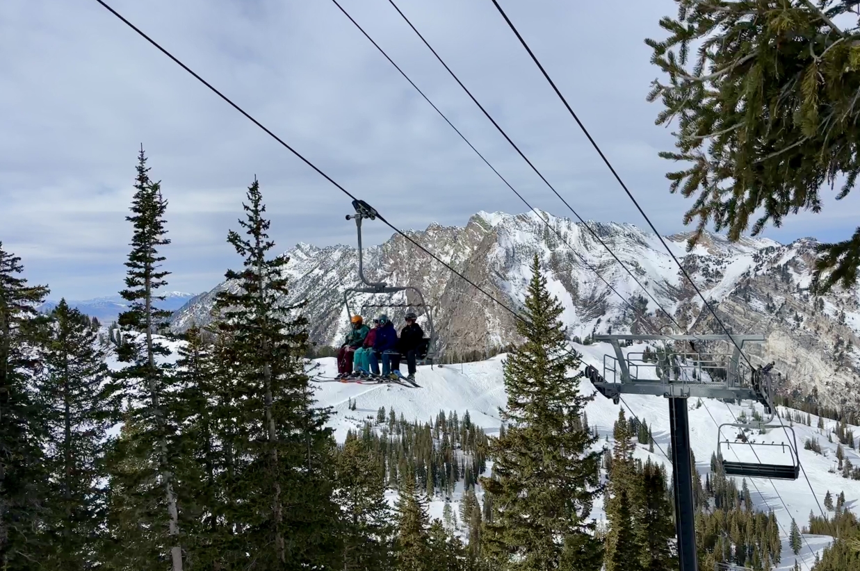 Ski lift chair moving through a forest with mountains in the distance.