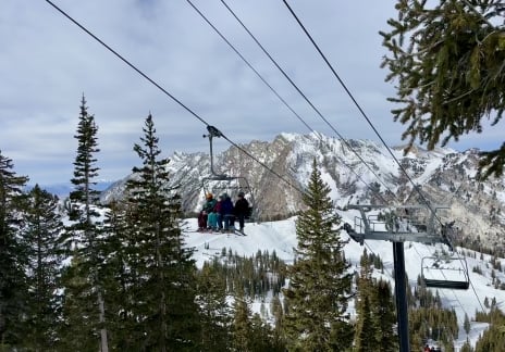 Ski lift chair moving through a forest with mountains in the distance.