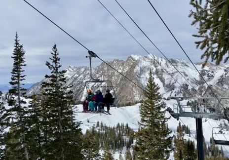 Ski lift chair moving through a forest with mountains in the distance.