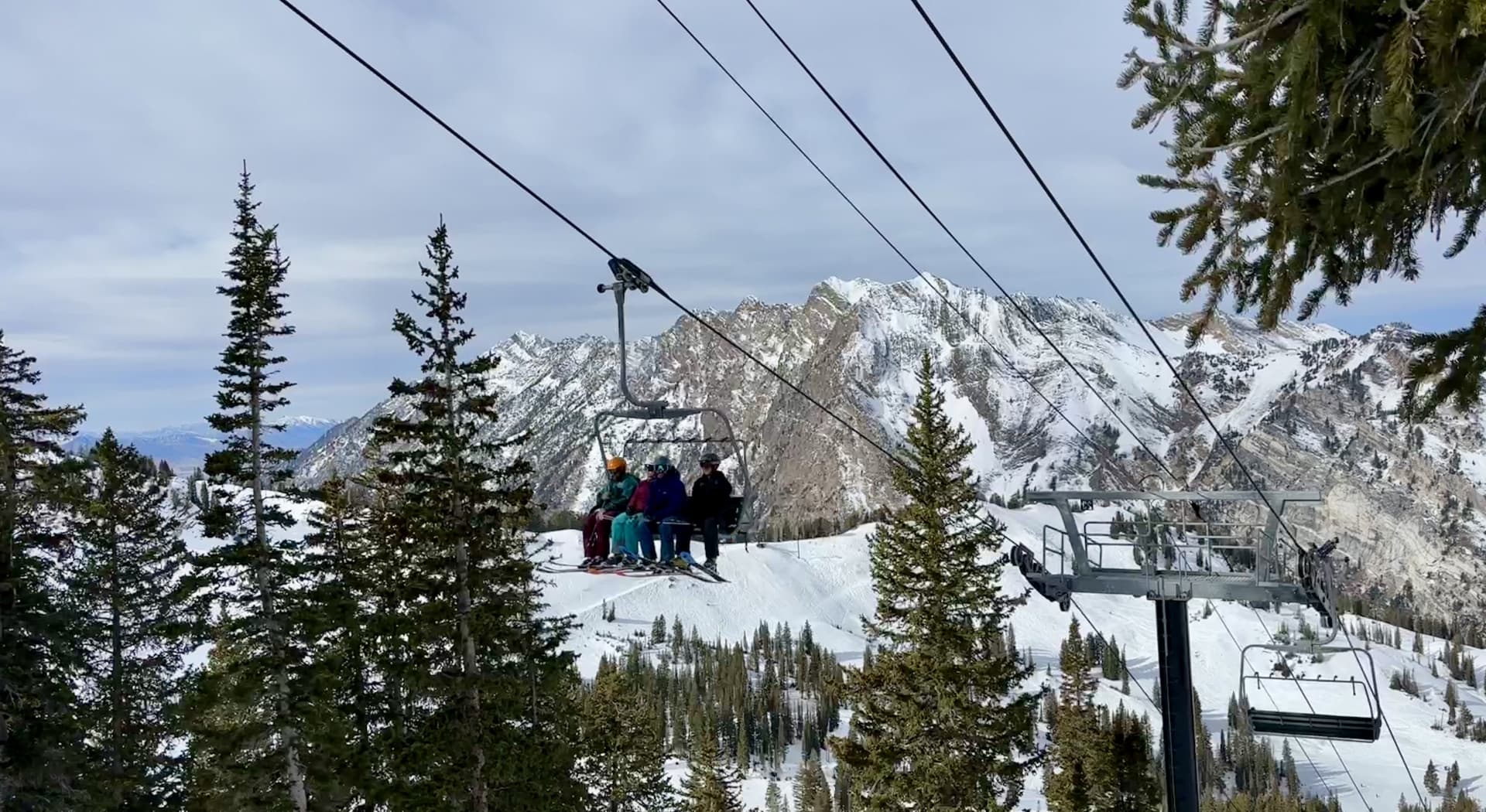 Ski lift chair moving through a forest with mountains in the distance.