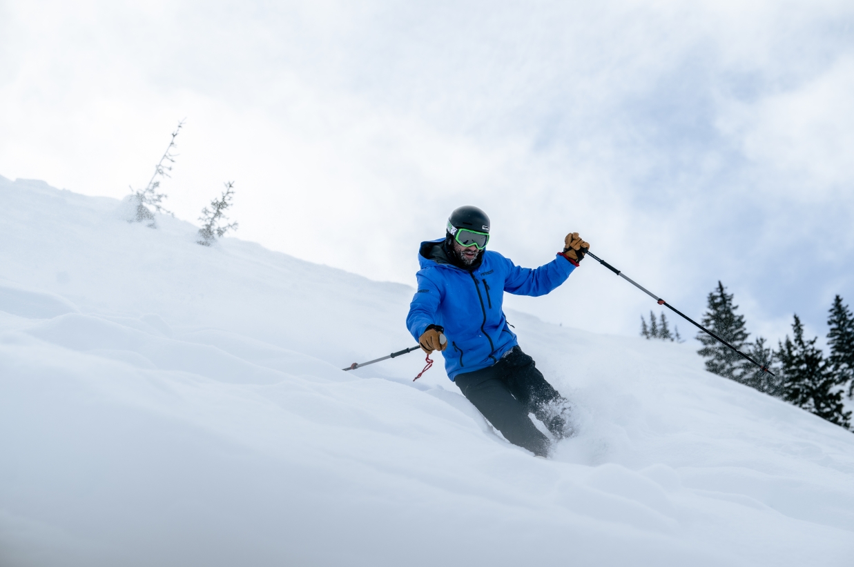 Skier in a blue jacket skiing down a snowy slope.