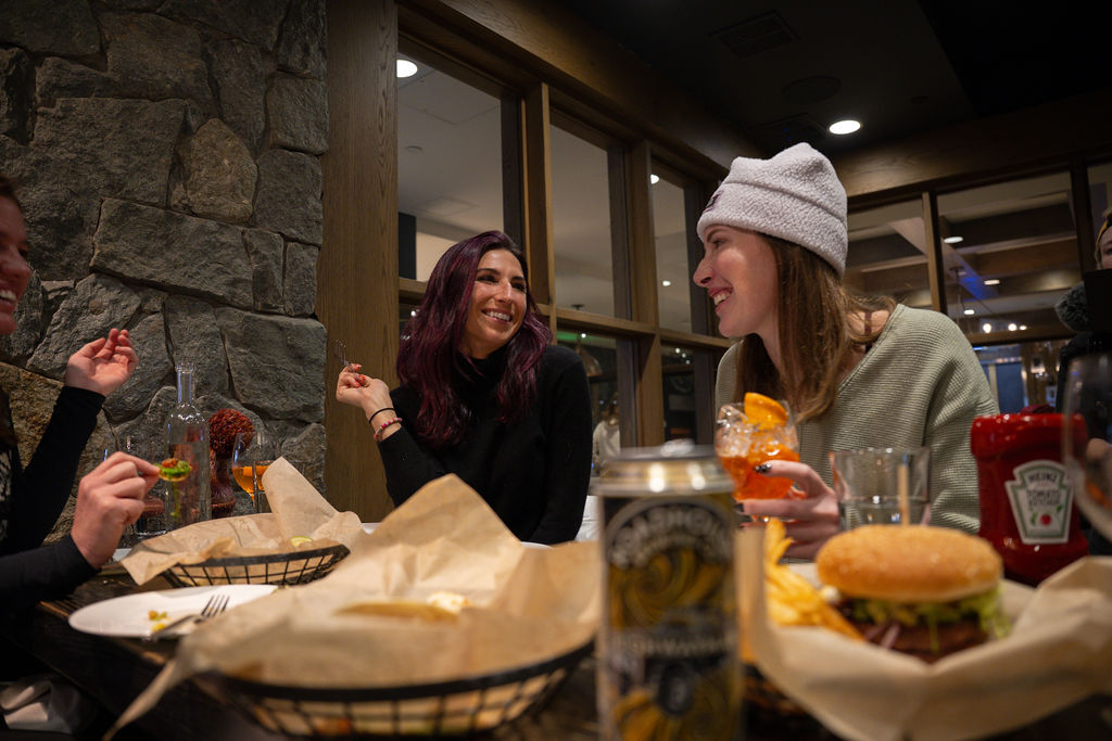 Two women laughing over dinner and drinks at a restaurant.