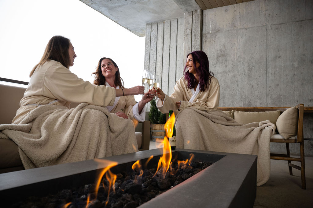 People in robes relaxing by an outdoor fire pit in the snow.