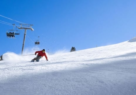 Skier carving turns on a wide, snowy run under a blue sky.