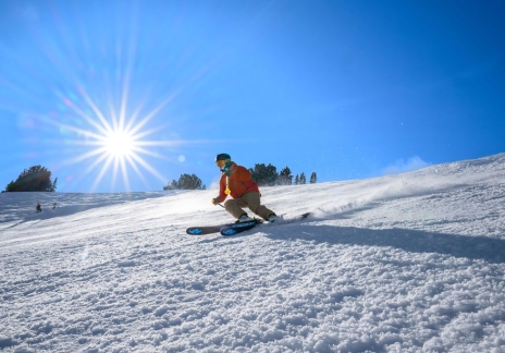Skier skiing on a groomed slope with a bright sunburst in the sky.