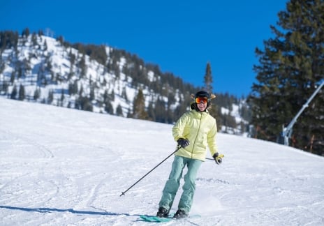 Skier in a yellow jacket standing on a sunny mountain slope.