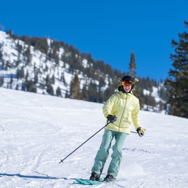 Skier in a yellow jacket standing on a sunny mountain slope.