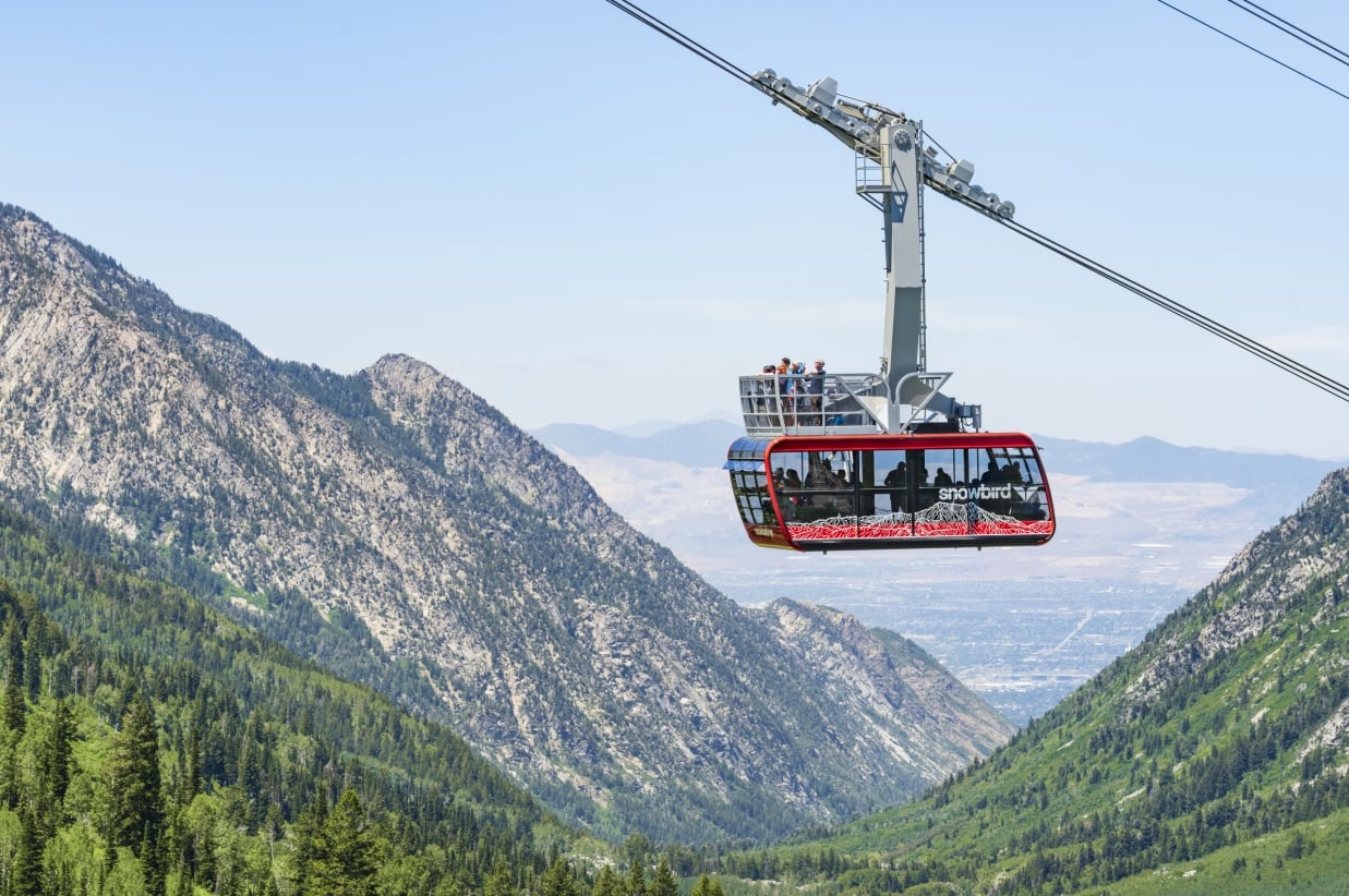 Red aerial tram car suspended on cables against mountains.