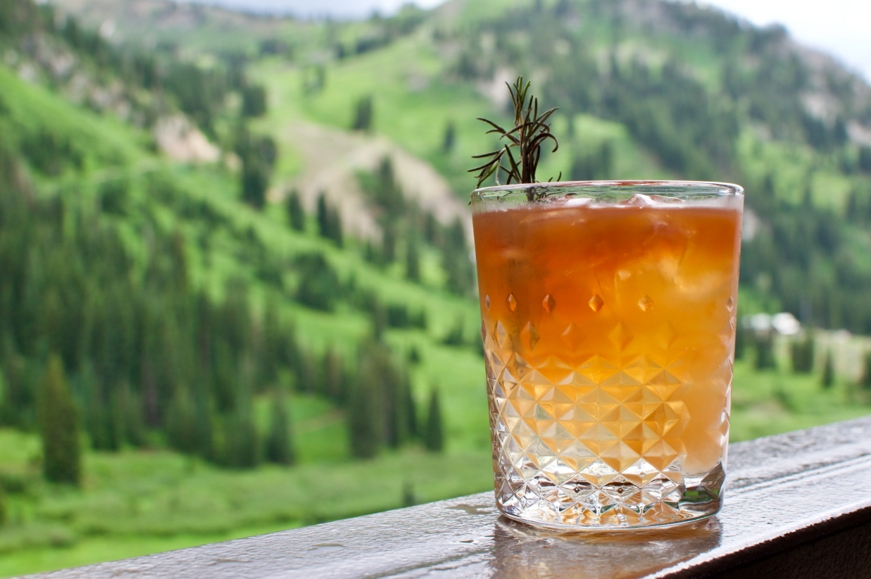 Close-up of an amber cocktail with a rosemary garnish on a railing.