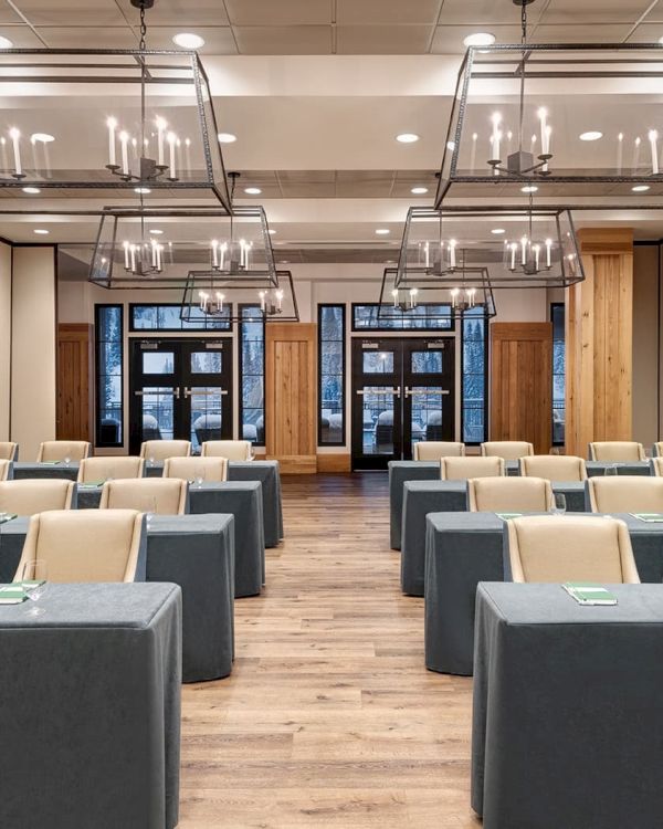 A modern conference room set with gray-covered tables, beige chairs, and hanging chandeliers.
