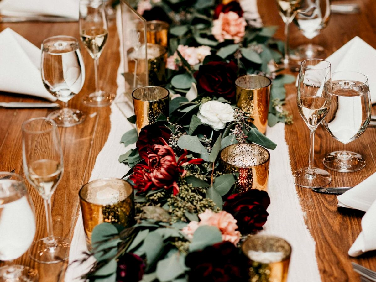 A formal banquet table with champagne flutes, folded napkins, and a lush floral centerpiece on a wood surface.