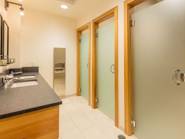 A bright modern bathroom with a double vanity, mirrors, and wooden doors leading to a wet area.