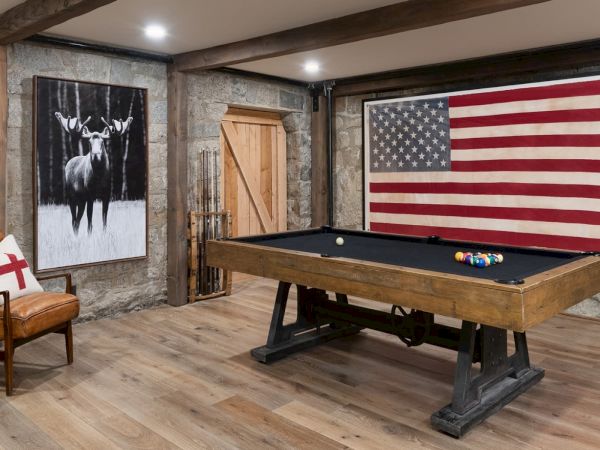 A rustic room with a wooden pool table, American flag wall art, a deer picture, and a leather chair.