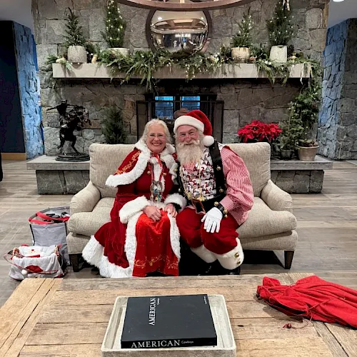 An older couple dressed for Christmas pose on a couch with garland and a coffee-table book titled “American Cowboy.”