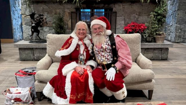 An older couple dressed for Christmas pose on a couch with garland and a coffee-table book titled &ldquo;American Cowboy.&rdquo;