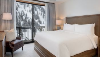 A cozy hotel room with a large bed, lamps, curtains, and a snowy mountain forest view through sliding doors.