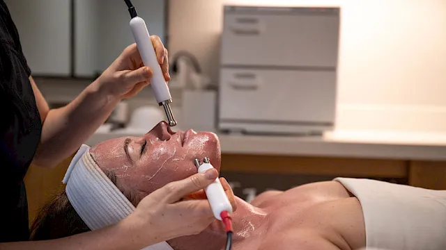 A clinician uses an electric skin-care device on a man&rsquo;s face during a spa treatment.
