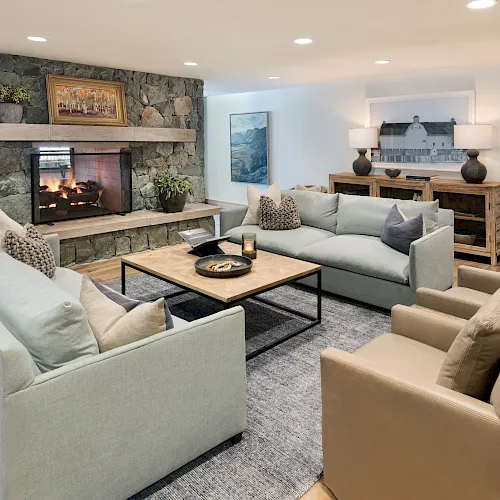 Cozy living room with a stone fireplace, plush sofas, wooden coffee table, lamps, and framed wall art.