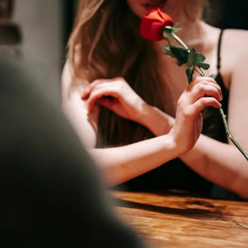 A woman holds a red rose by its stem, likely decorating or offering it.