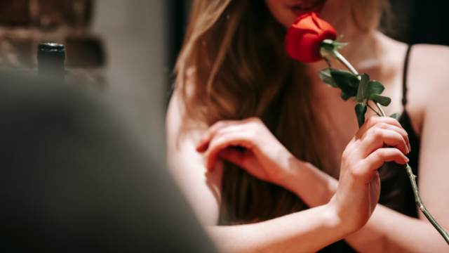 A woman holds a red rose by its stem, likely decorating or offering it.