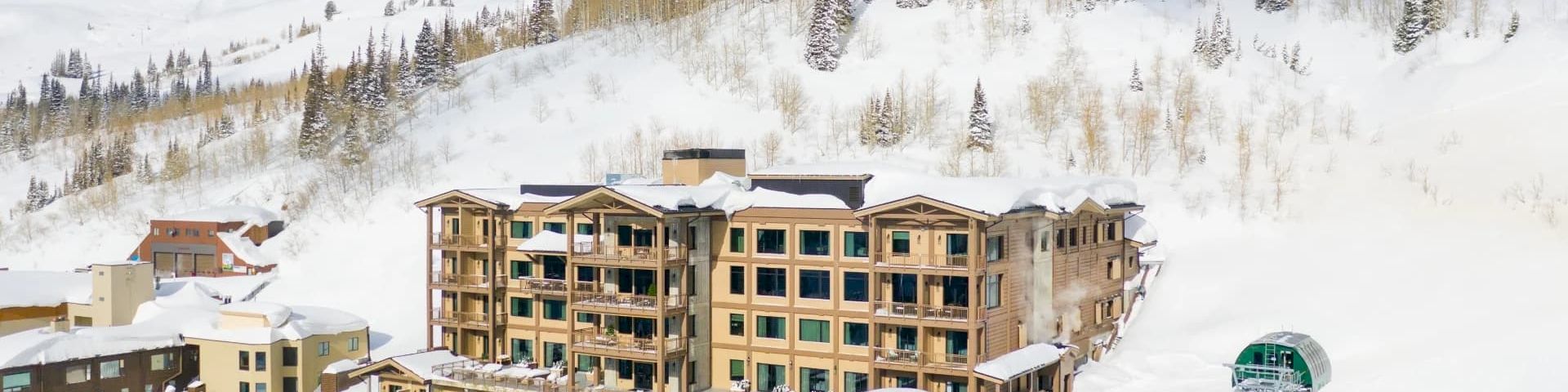 A snowy mountain resort with an outdoor pool and ski lifts, surrounded by alpine peaks and pine trees.