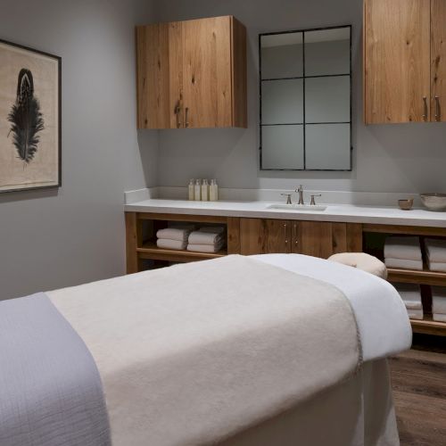 Modern bathroom with a wooden vanity, double faucets, stocked bottles, and folded towels beneath the sink.