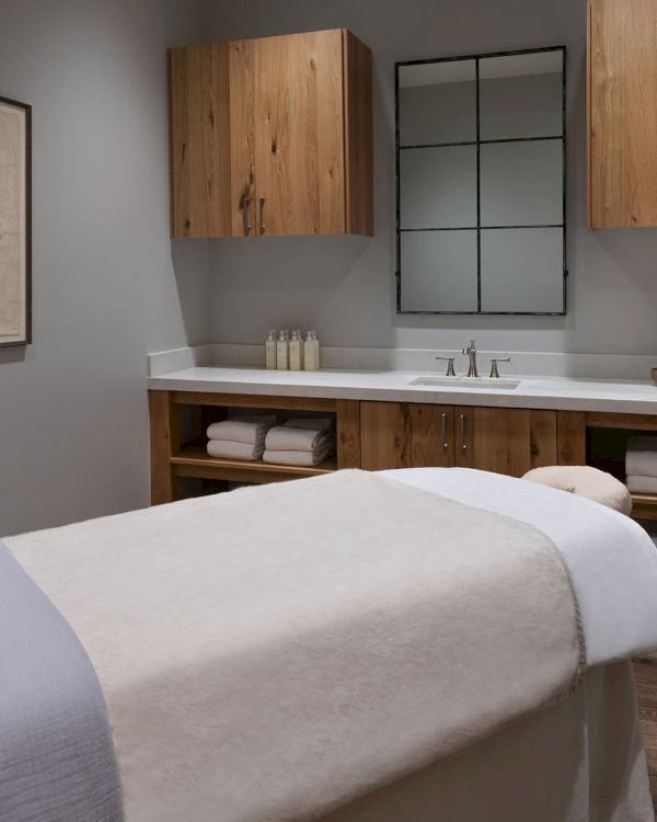 Modern bathroom with a wooden vanity, double faucets, stocked bottles, and folded towels beneath the sink.